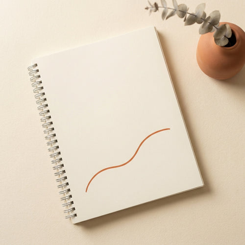 Closed printable workbook on warm cream surface, soft side-light, hands resting on cover